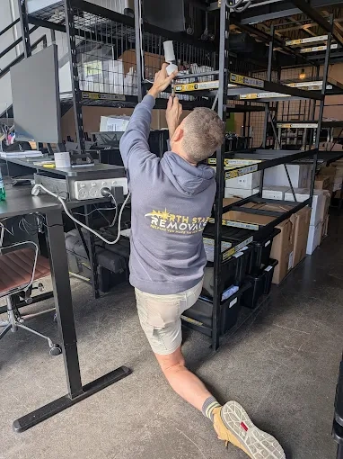Andy in a North Star Removals hoodie reaching up to shelving during an office fit-out